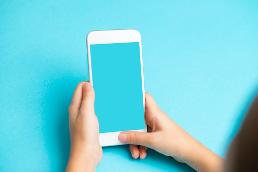 Child using mobile phone. Looking at mobile app, mobile web or game. Phone display is a blue. Blue background.