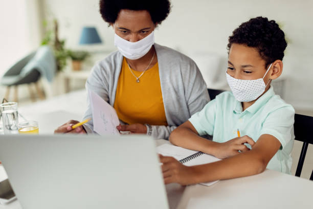 istock Black boy using laptop while studying at home with is mother due to COVID-19 epidemic. 1272853408