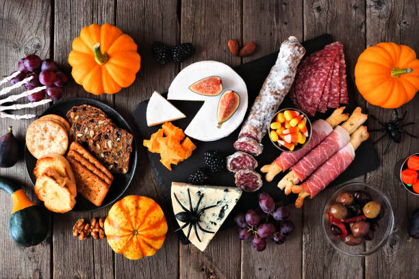 Halloween charcuterie top view table scene against a dark wood background Halloween theme charcuterie table scene against a dark wood background. Assorted cheese and meat appetizers. Top view. prosciutto brie stock pictures, royalty-free photos & images