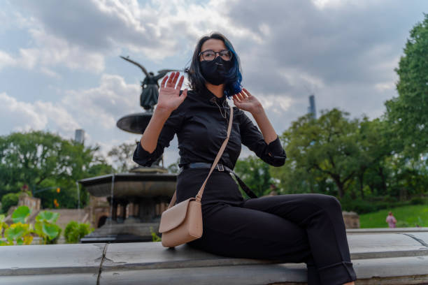 Teenage girl sitting on a fountain at Bethesda Terrace in Central Park deserted because of the pandemic and social distancing. She is wearing a protective face mask because of COVID-19 epidemic. A 17-years-old teenage girl wearing protective mask in Central Park, Manhattan, NY black hair emo girl stock pictures, royalty-free photos & images