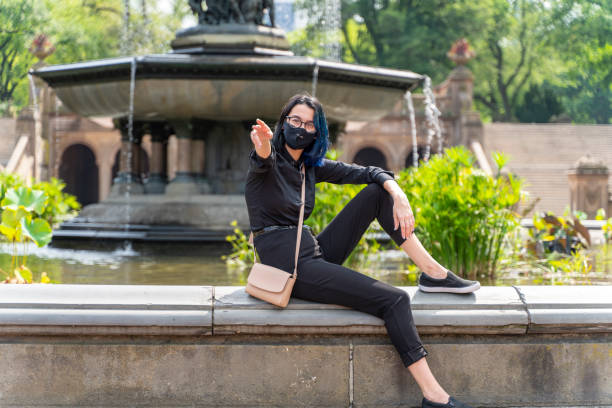Teenage girl sitting on a fountain at Bethesda Terrace in Central Park deserted because of the pandemic and social distancing. She is wearing a protective face mask because of COVID-19 epidemic. A 17-years-old teenage girl wearing protective mask in Central Park, Manhattan, NY black hair emo girl stock pictures, royalty-free photos & images