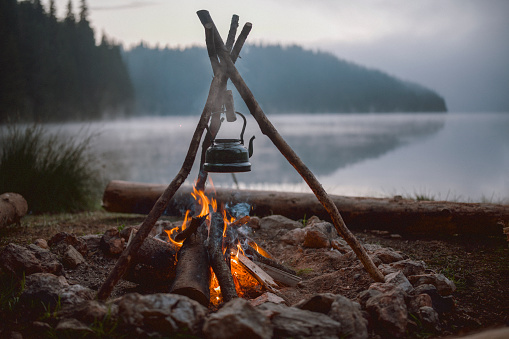 Beautiful photo of a campfire and a vintage teapot with a herbal tea on it with the background of the mountains