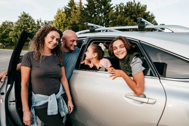 kaukasische familie in der nähe des autos, das in die kamera schaut. zwei kinder und eltern lächeln. - family four people smiling autumn stock-fotos und bilder