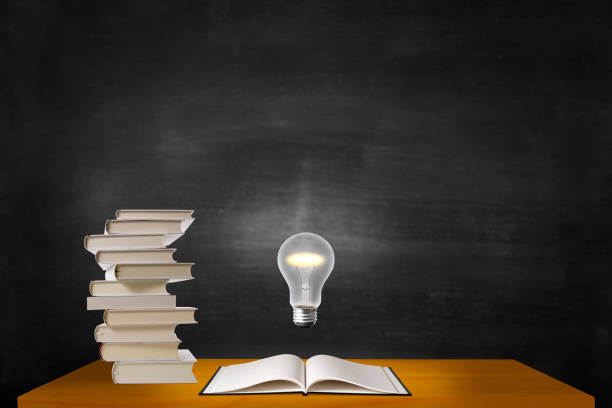 istock Light bulb glowing in mid-air over the stacked blank books on a desk. 1272909971