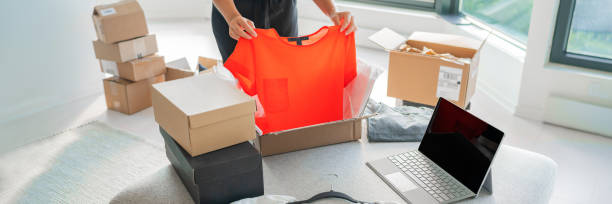 online-shop verkaufe kleidung auf website und arbeite von zu hause aus mit laptop-e-commerce-geschäften. frau verpackung neue kleidung mode kauf in versandpakete für die lieferung. panorama-banner - selling e commerce sale internet stock-fotos und bilder