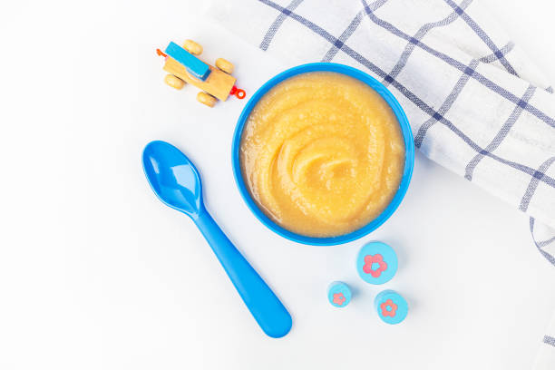 Baby food. Fresh homemade applesauce. Blue bowl with fruit puree on fabric and kids toys on table. The concept of proper nutrition and healthy eating. Organic and vegetarian food. Copy space for text comida para bebés. puré de manzana casero fresco. tazón azul con puré de frutas en tela y juguetes para niños en la mesa. el concepto de nutrición adecuada y alimentación saludable. comida orgánica y vegetariana. copiar espacio para texto