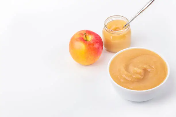 Fresh homemade applesauce in white bowl and jar with fruit puree on white table. The concept of proper nutrition and healthy eating. Organic and vegetarian food. Baby food. Copy space for text