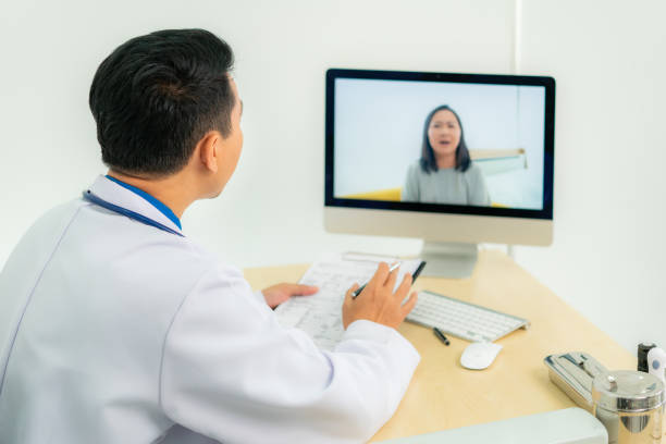 istock Asian man doctor wears white coat and headset speaking videoconferencing on laptop computer using online video call consultation app. Remote medical help for distance patient, telemedicine. 1272924148