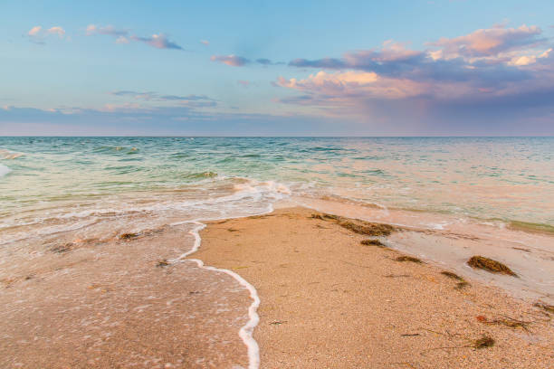 istock Seashore at sunset, sand is washed from two sides by waves, clouds in the sky 1272924878