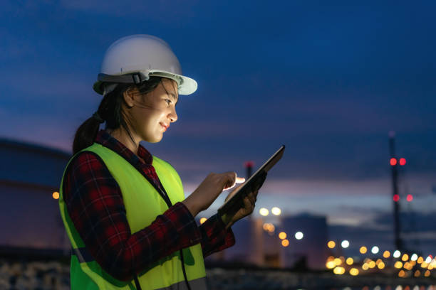 asian woman petrochemical engineer working at night with digital tablet inside oil and gas refinery plant industry factory at night for inspector safety quality control. - engineer occupation women industrial imagens e fotografias de stock