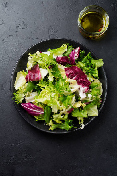 istock Fresh leaves of different salads in ceramic plate on black stone background. Selective focus. Top view. Copy space. 1272929804