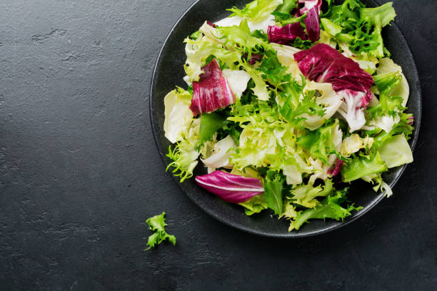 Fresh leaves of different salads in ceramic plate on black stone background. Selective focus. Top view. Copy space.
