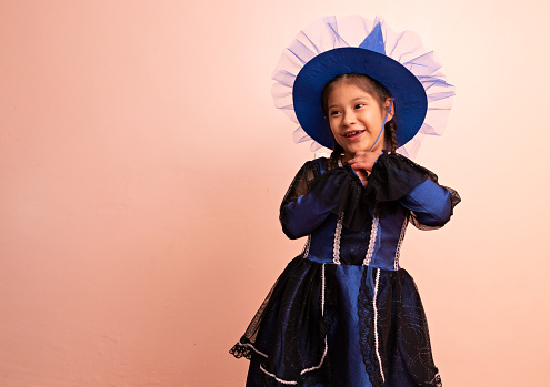 little girl disguised in a blue witch costume, in front of a pink background, posing and smiling