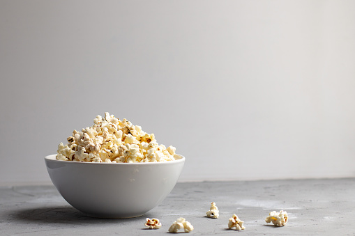 popcorn in a white bowl on grey table with few popcorn beside bowl. Copyspace