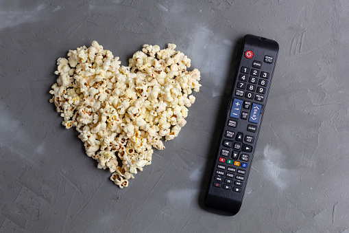 Popcorn in the shape of a heart and TV remote on grey stone background. Love movie. top view.
