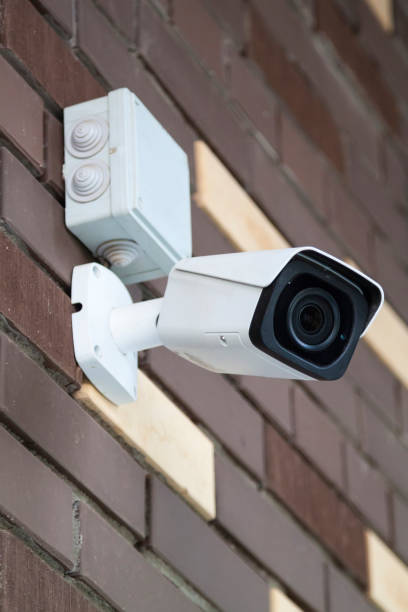 istock Closed-circuit television camera mounted on brick wall. CCTV security camera outdoors. 1272936019
