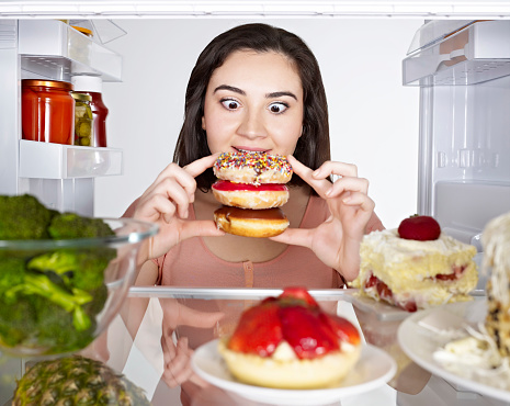 Young woman looking at donuts from inside of a fridge.