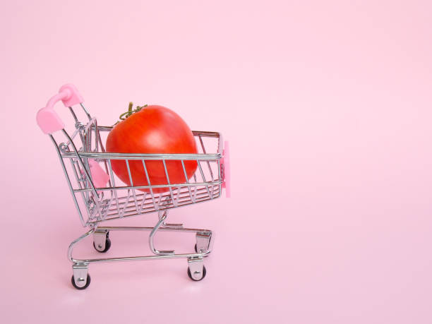 Small shopping cart with big tomato on pink background Small grocery cart with big unusual tomato on pink background unusual basket stock pictures, royalty-free photos & images