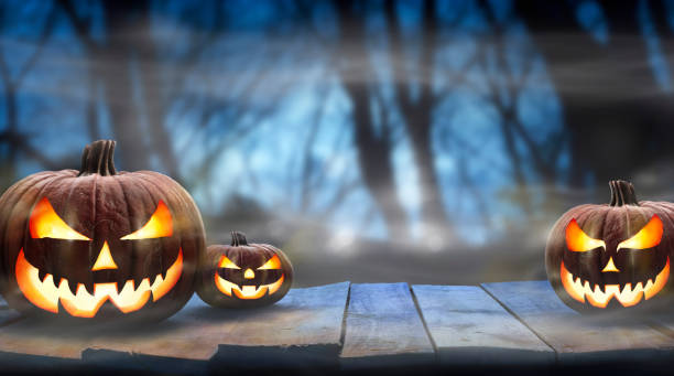 istock Three spooky halloween pumpkins, Jack O Lantern, with evil face and eyes on a wooden bench. 1272937090