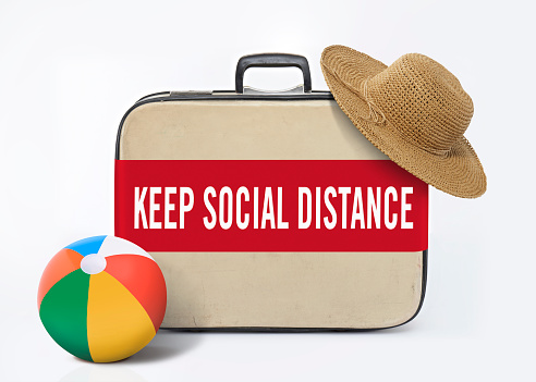 Straw hat on a retro luggage with a banner quoting “Keep social distance”
