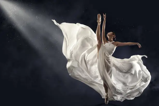 Ballerina Jumping doing Splits in White Silk Dress, Modern Ballet Dancer in Pointe Shoes, Fluttering Waving Cloth, over Gray Background