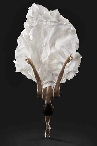 Bailarina Graceful Jump en vestido de seda blanco, ballet Dancer Pointe zapatos en tela de aleteo, fondo negro photo