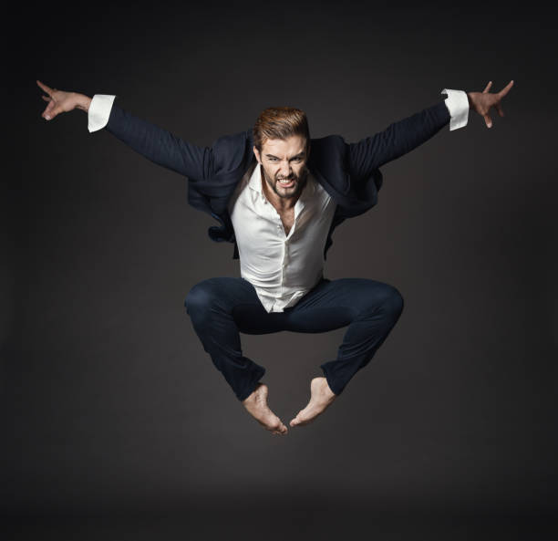 handsome man in business suit jumping in air, full length young ballet dancer over black background - men businessman jumping levitation imagens e fotografias de stock