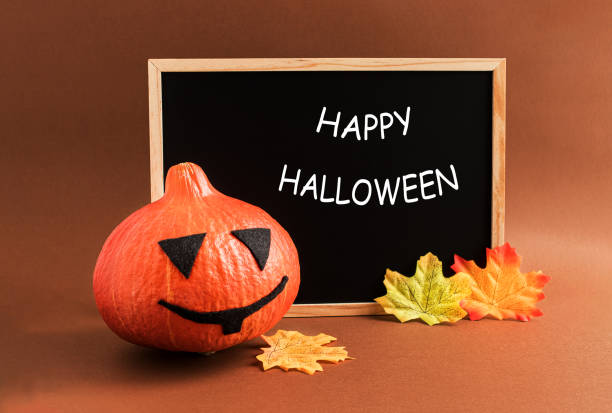 istock Decorative pumpkin, autumn leaves and a black message Board with a welcome message on a brown background. The concept of the holiday of Halloween 1272939512