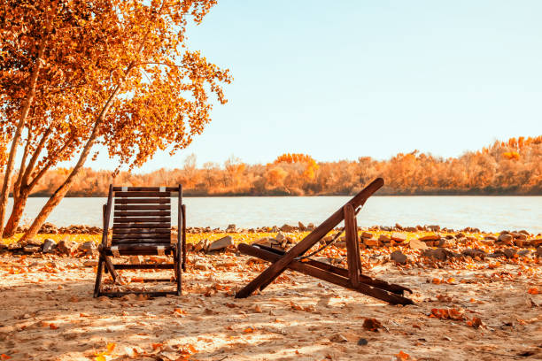 Autumn landscape with two chairs on the sandy river bank.