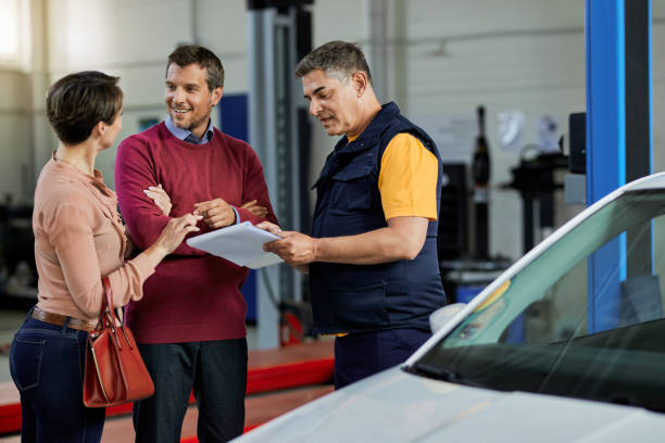 Happy couple talking to their auto mechanic in a workshop.