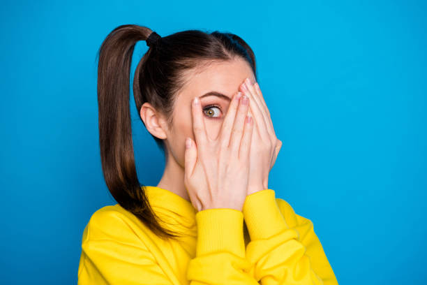 foto de close-up de mulher bonita dois braços de cauda escondendo olhos olhar medo assistir cinema filme de filme de terror usar moletom amarelo pullover isolado fundo de cor azul brilhante - film tails - fotografias e filmes do acervo