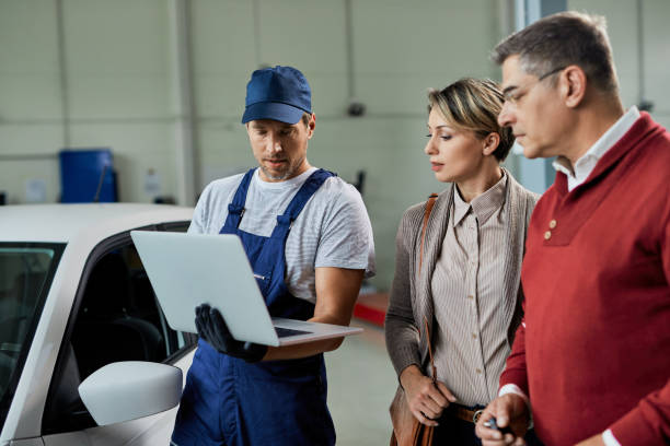 istock Auto mechanic using laptop while talking to a couple in auto repair shop. 1272946365