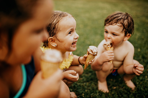 Siblings eating ice cream near swimming pool in back yard