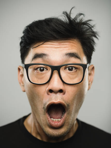 Portrait of a real chinese man with surprised expression Close up portrait of asian mid adult man with surprised expression against white gray background. Vertical shot of chinese real people with mouth open in studio with black hair and glasses. Photography from a DSLR camera. Sharp focus on eyes. confusion raised eyebrows human face men stock pictures, royalty-free photos & images