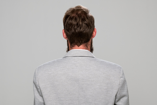 Rear view of mid adult man standing against grey background.