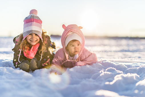 Beautiful sisters enjoying winter snow on sunset. Toddler girl is 4 years old, while baby is 6 months old.