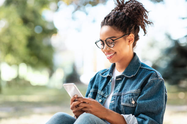 istock Black Girl With Smartphone Using Mobile App Sitting In Park 1272958127