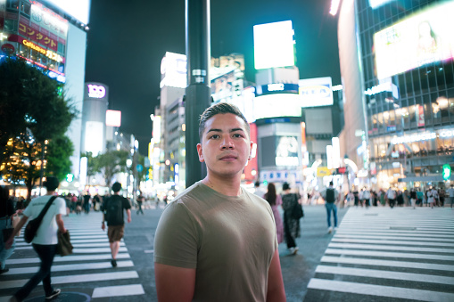 Portrait of a young man at night at the Shibuya Crossing in Tokyo.
Standing in the bright night streets of neon.