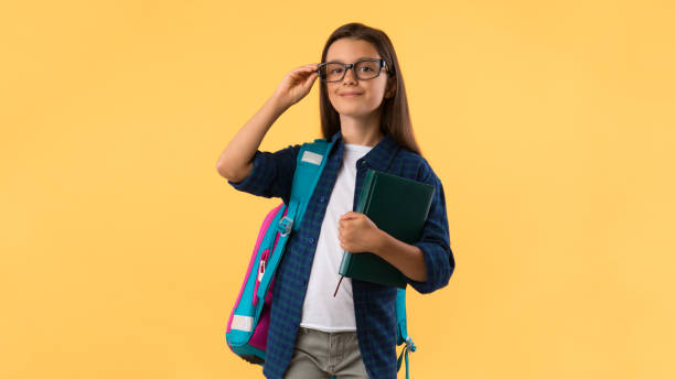 chica sonriente sosteniendo libro de texto en el fondo del estudio - schoolgirl pre adolescent child school children book bag fotografías e imágenes de stock