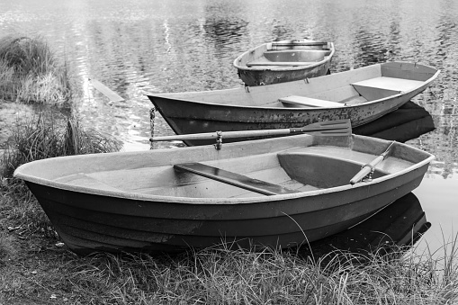 Rowboats are at coast of a still lake, black and white photo