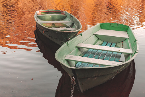 Two small rowboats are anchored at coast of a still lake