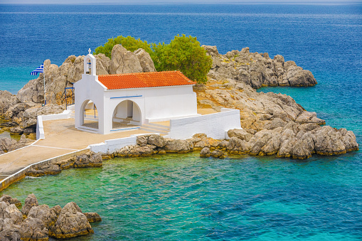 classical white greek church on a small rocky island in Agios Isidoros, Greece