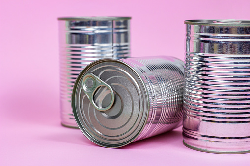 Tinned food and metal cans storage on light pink background.