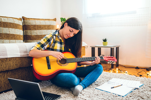 Young woman is composing a song on an acoustic guitar at home.