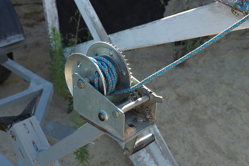 part of a gray iron winch with a blue rope on the street