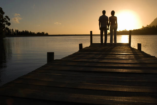 istock Couple standing on dock by lake holding hands back view 1272965799