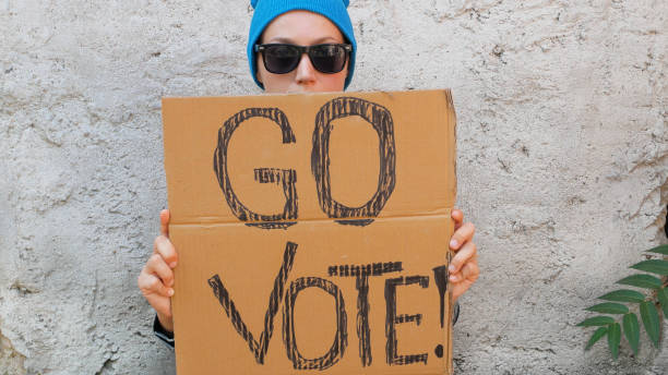 woman shows cardboard with go vote sign on brick wall urban background. voting concept. make political choice, elections - jovens a votar imagens e fotografias de stock