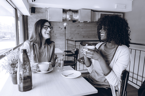 Two young multi-ethnic women drinking coffee in cafe.