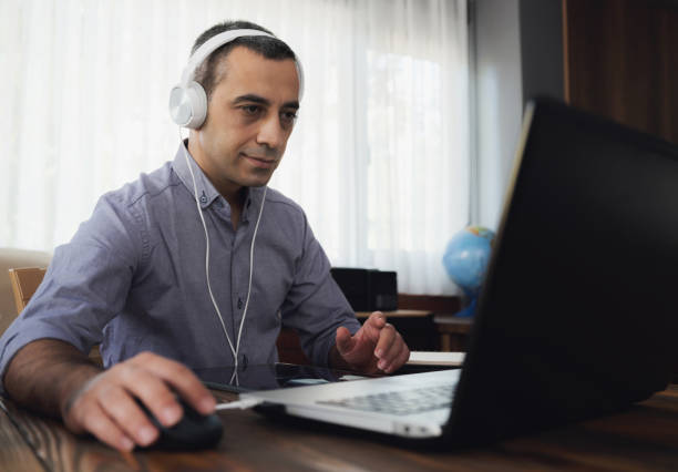 istock Man Is Working Online In Home Office Using His Laptop Computer, Joining Webinar And Taking Notes On Digital Tablet 1272968004