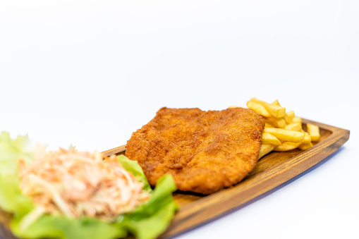 Fried chicken breast on the wooden board with a salad from cabbage and French fries on the side isolated on white background
